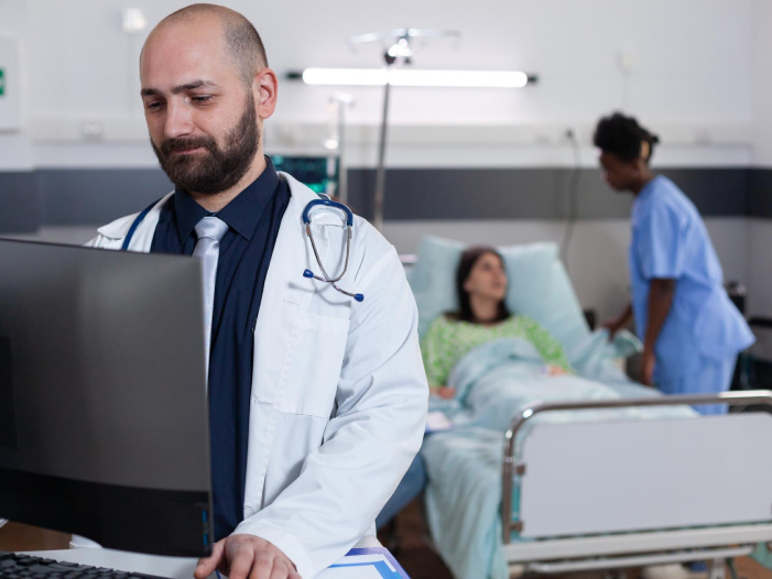 Doctor consultando información en computadora mientras atiende a un paciente en la sala